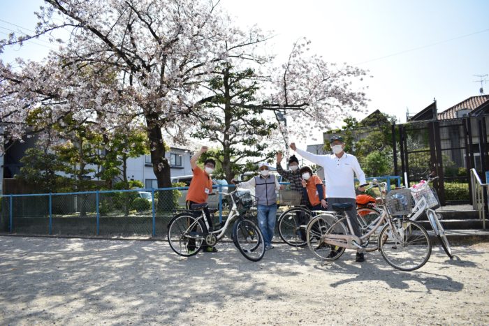 桜の下で腕を上げる男女と自転車